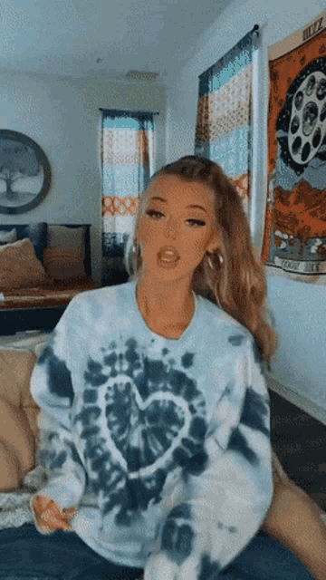 a woman wearing a blue tie dye sweater with a heart on it