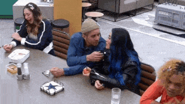 a man and woman are sitting at a table with other people . the woman has blue hair .