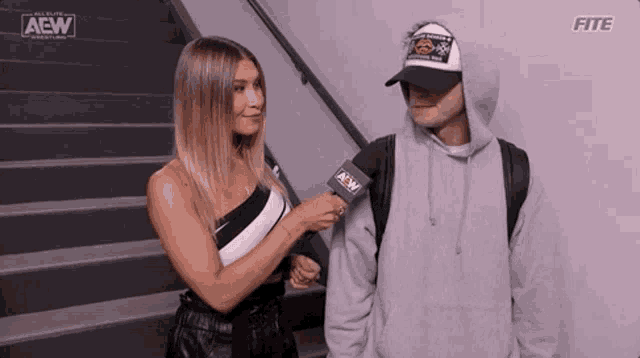 a woman is talking to a man with a microphone while standing next to a staircase .