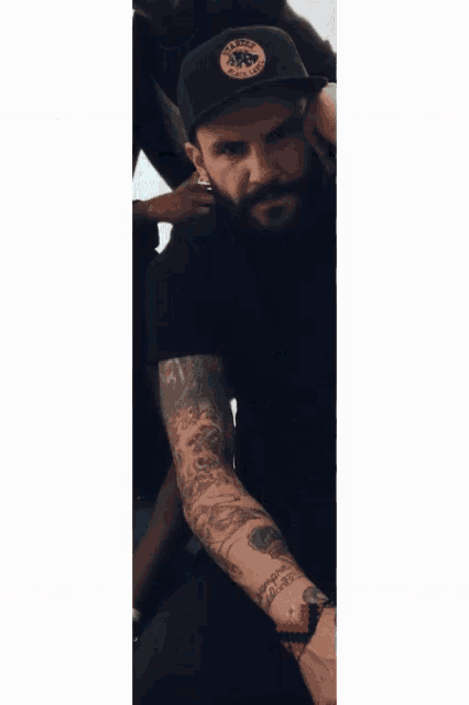 a man with a beard and tattoos wearing a black shirt and hat