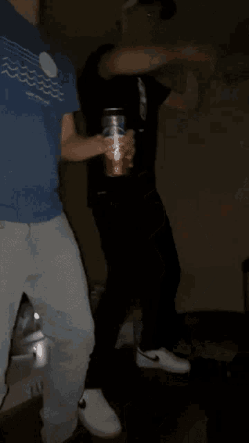 a man in a blue shirt is standing next to another man holding a can of beer .