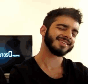 a man with a beard is smiling in front of a tv that says utosqu