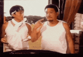 two men in white tank tops are standing next to each other and talking to each other .