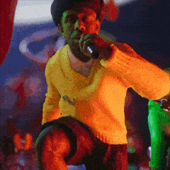 a man in a yellow sweater is singing into a microphone in front of a crowd