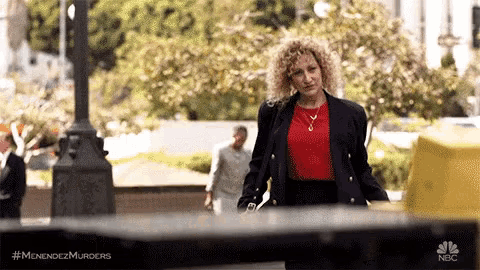 a woman in a red shirt and black jacket is walking down a sidewalk .