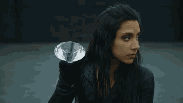 a woman in black gloves holds a large diamond in her hand