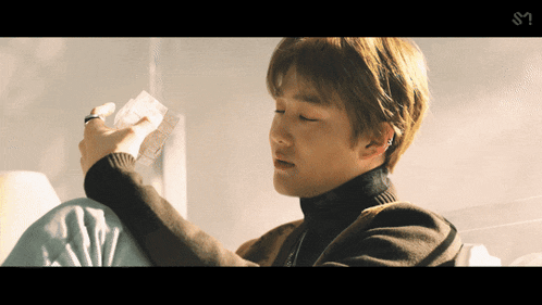 a man in a turtleneck is holding a piece of paper with the letter s on the bottom