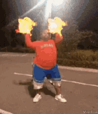 a man in a red shirt and blue shorts is holding fire in his hands .