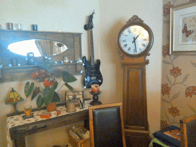 a guitar is hanging on a wall next to a grandfather clock that shows the time as 8:17