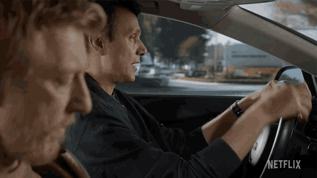 a man driving a car with a netflix logo on the bottom right