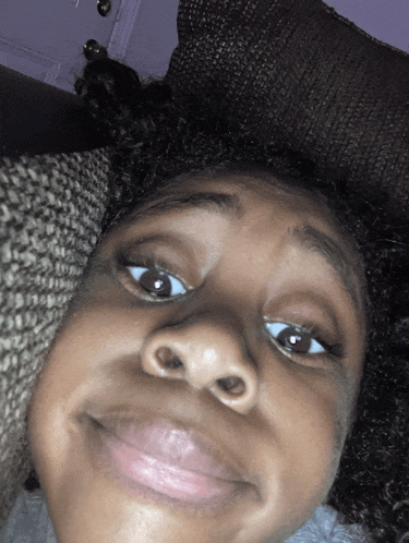 a close up of a person 's face with a pillow behind her