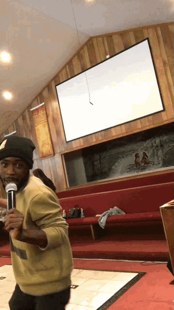 a man singing into a microphone in a church with a sign on the wall that says " jesus loves you "