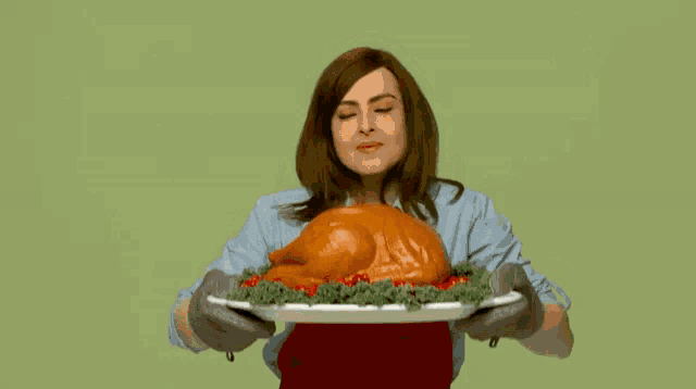 a woman in an apron is holding a roasted turkey on a tray