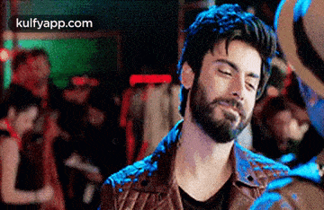 a man with a beard wearing a leather jacket is standing in a crowded room .