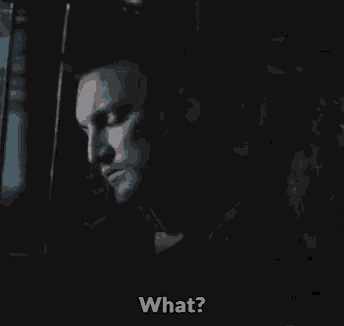 a man is sitting in a dark room talking on a cell phone and asking what .