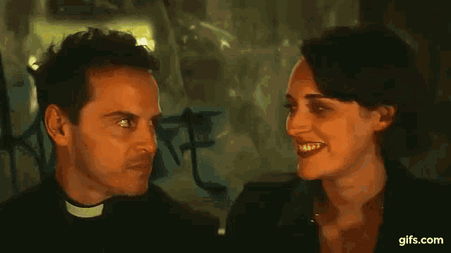 a priest is making a funny face while talking to a woman in a dark room .