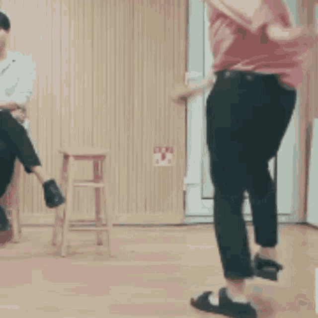 a man in a pink shirt is squatting on the floor while another man sits on a stool in a room .