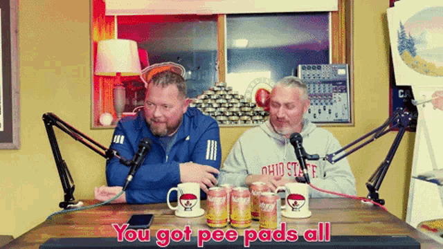 two men are sitting at a table talking into microphones with the words you got pee pads all