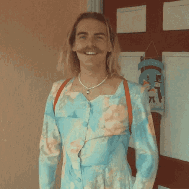 a man wearing a dress and a pearl necklace is smiling