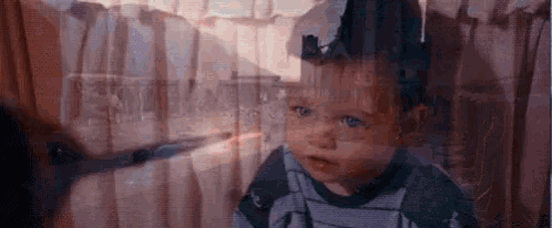 a baby is looking out of a window with a reflection of a person in the window .