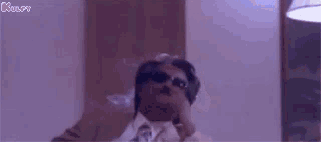 a man in a suit and tie is smoking a cigarette while wearing sunglasses .