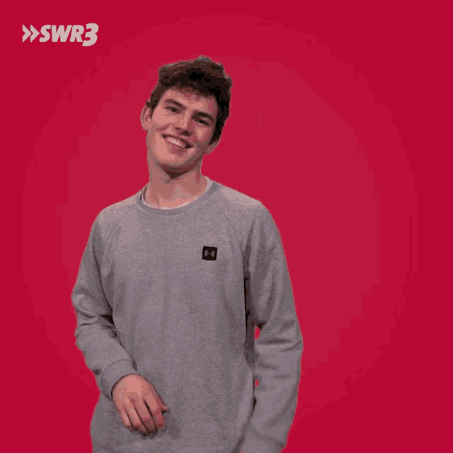 a man wearing a gray sweatshirt is dancing in front of a red background with swr3 written on it