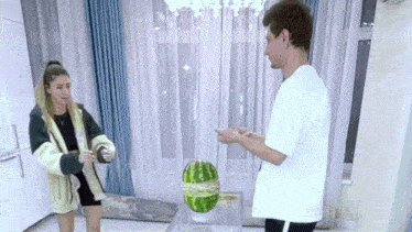 a man and a woman are standing next to a watermelon on a table .