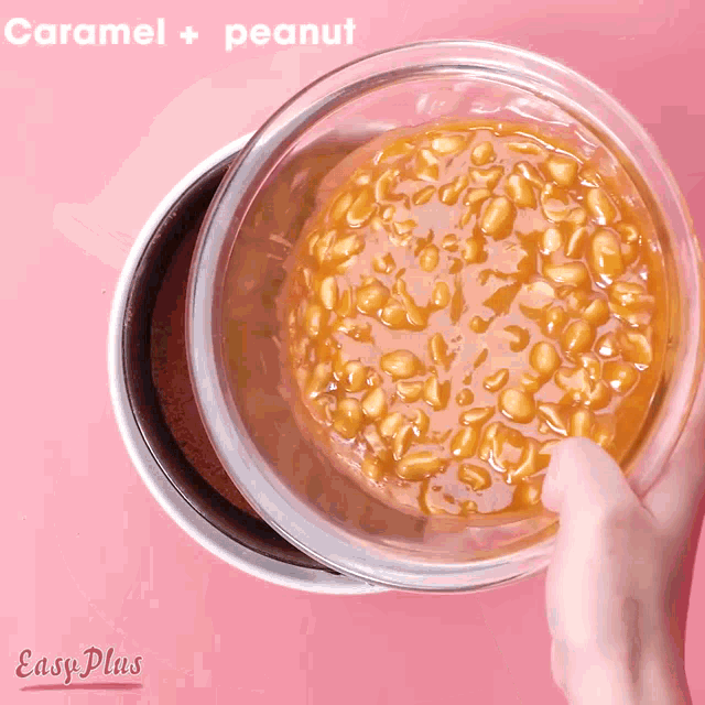 a person is holding a bowl of caramel and peanut on a pink surface