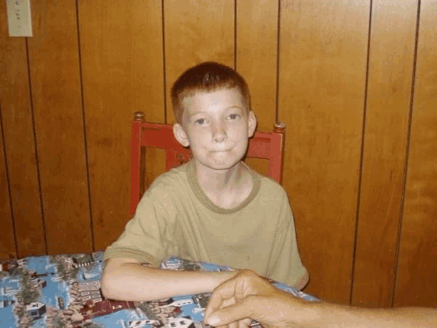 a young boy is sitting at a table with a hand reaching out towards him