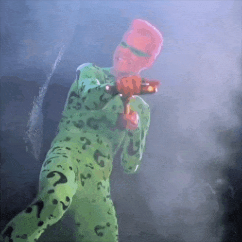 a man in a green suit with a question mark on it holds a gun