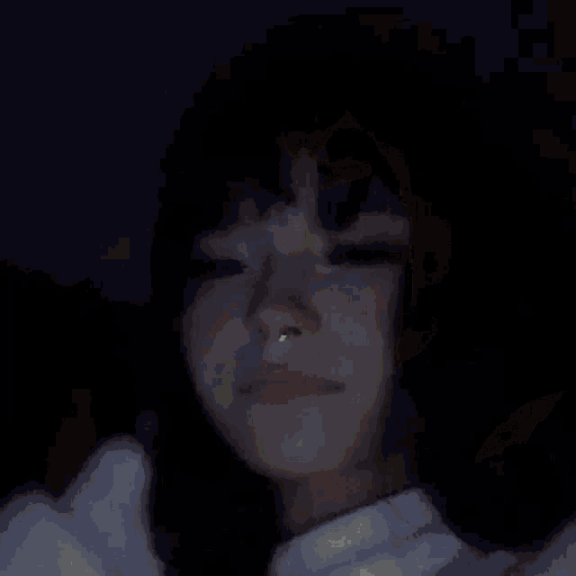 a woman with a nose ring and a ring on her finger is looking at the camera in the dark .