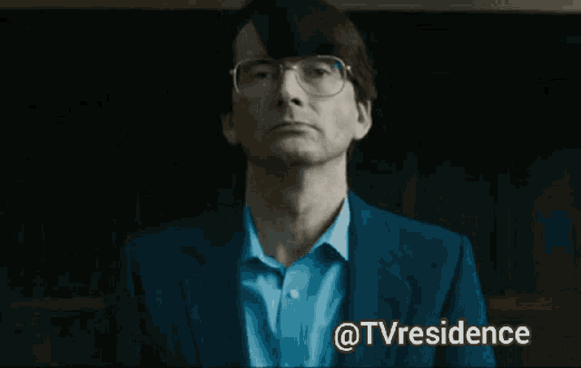 a close up of a man wearing glasses and a blue shirt with the words @tvresidence above him