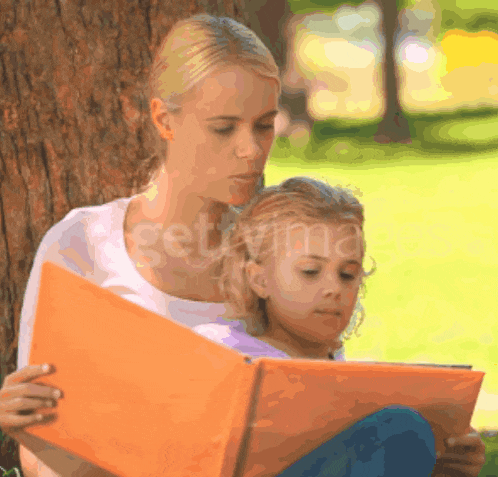 a woman is reading a book to a little girl while sitting under a tree ..