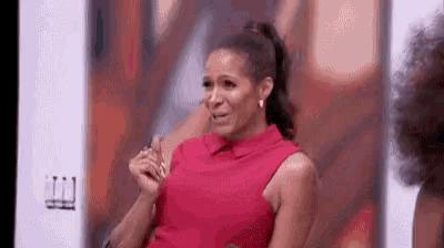 a woman in a red dress is sitting in front of a wall and crying .