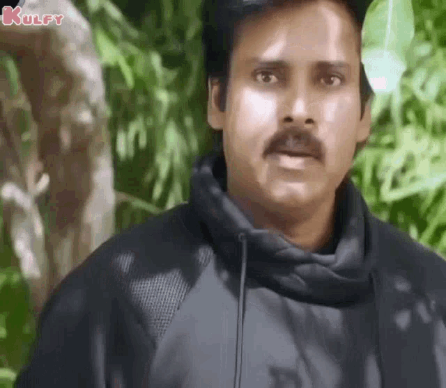 a man with a mustache is wearing a black hoodie and looking at the camera .