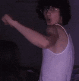 a man wearing glasses and a white tank top is standing in the dark