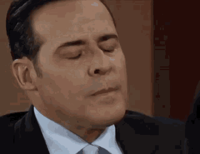 a man in a suit and tie is making a face with his eyes closed .