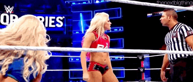 two women are wrestling in a ring and a referee is standing in the ring .