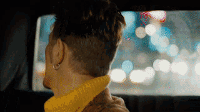 a man in a yellow sweater is looking out the window of a car
