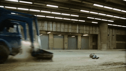 a man is laying on the ground in front of a blue truck that is driving by
