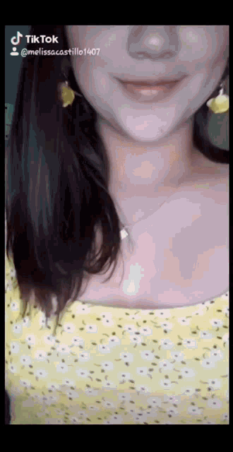 a close up of a woman 's face with a yellow top and earrings