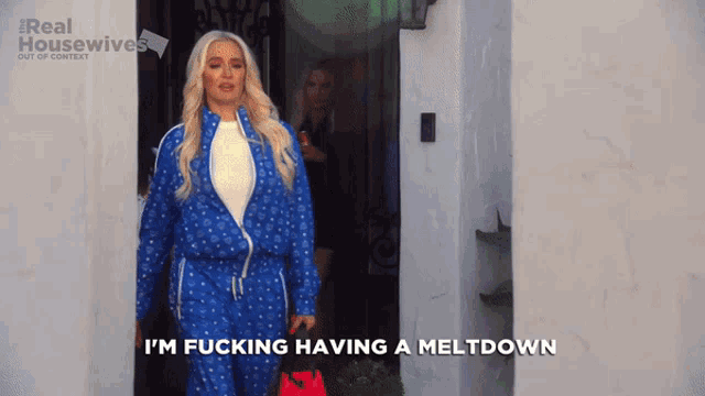 a woman in a blue tracksuit says i 'm fucking having a meltdown in front of a white wall