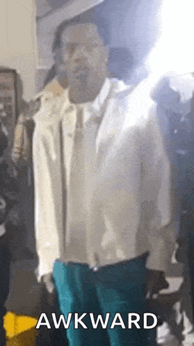 a man in a white jacket and blue pants is standing in front of a crowd with the word awkward on the bottom .