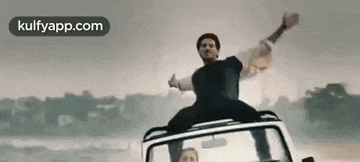 a man is sitting on top of a car giving a thumbs up .