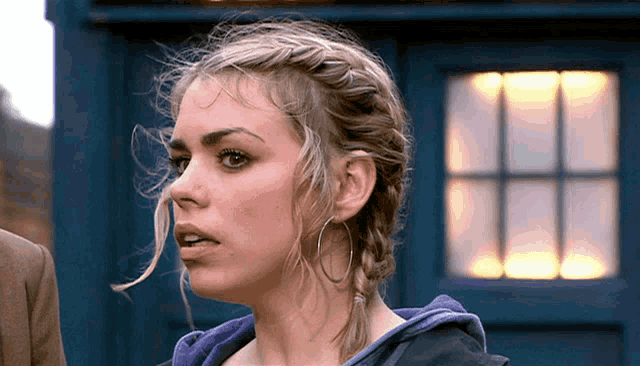 a woman wearing hoop earrings is standing in front of a blue police box