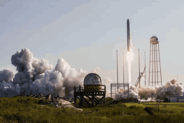 a rocket is being launched into space with smoke coming out of it and a water tower in the background