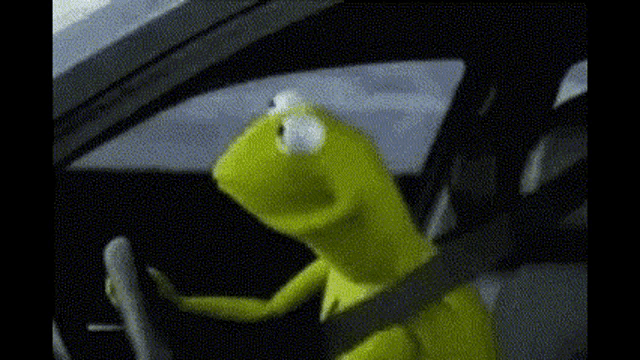 a kermit the frog is sitting in the driver 's seat of a car and looking out the window .