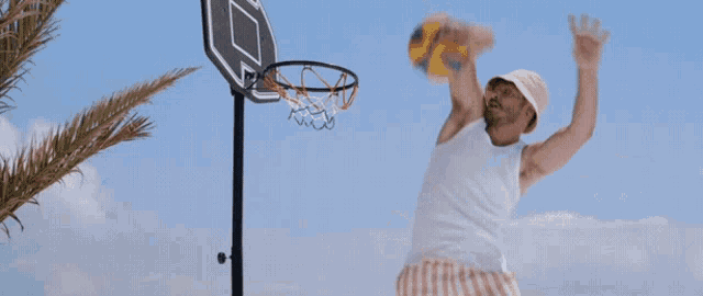 a man in a white tank top and striped shorts is playing basketball on the beach