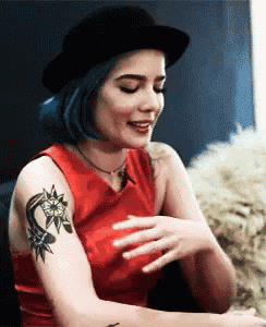 a woman with blue hair and a tattoo on her arm is wearing a black hat .