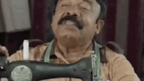 a man with a mustache is sitting at a sewing machine .